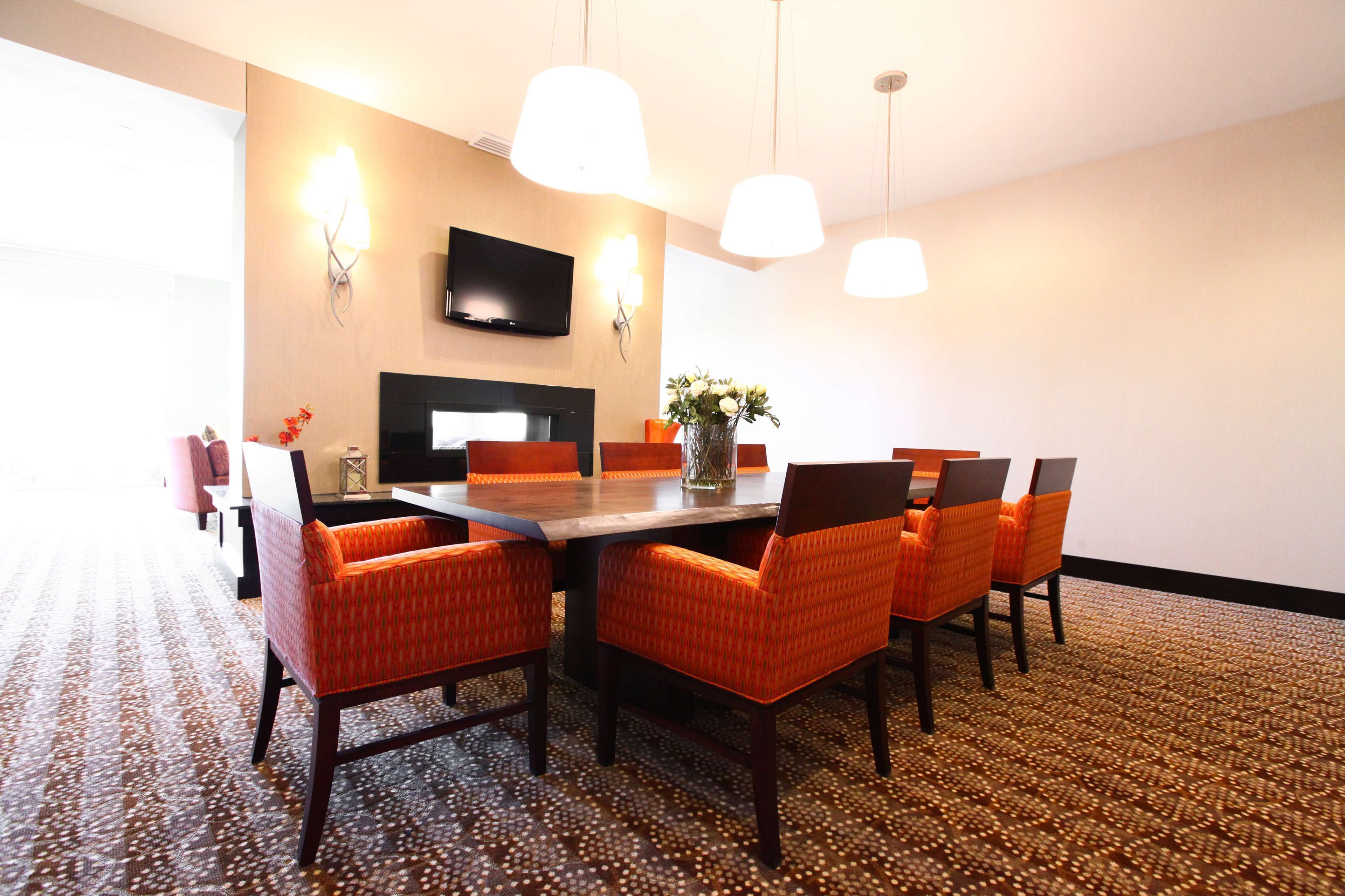 A conference room with a long table, six orange chairs, a vase with flowers, a flat-screen TV, and pendant lights.