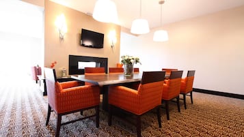 A conference room with a long table, six orange chairs, a vase with flowers, a flat-screen TV, and pendant lights.