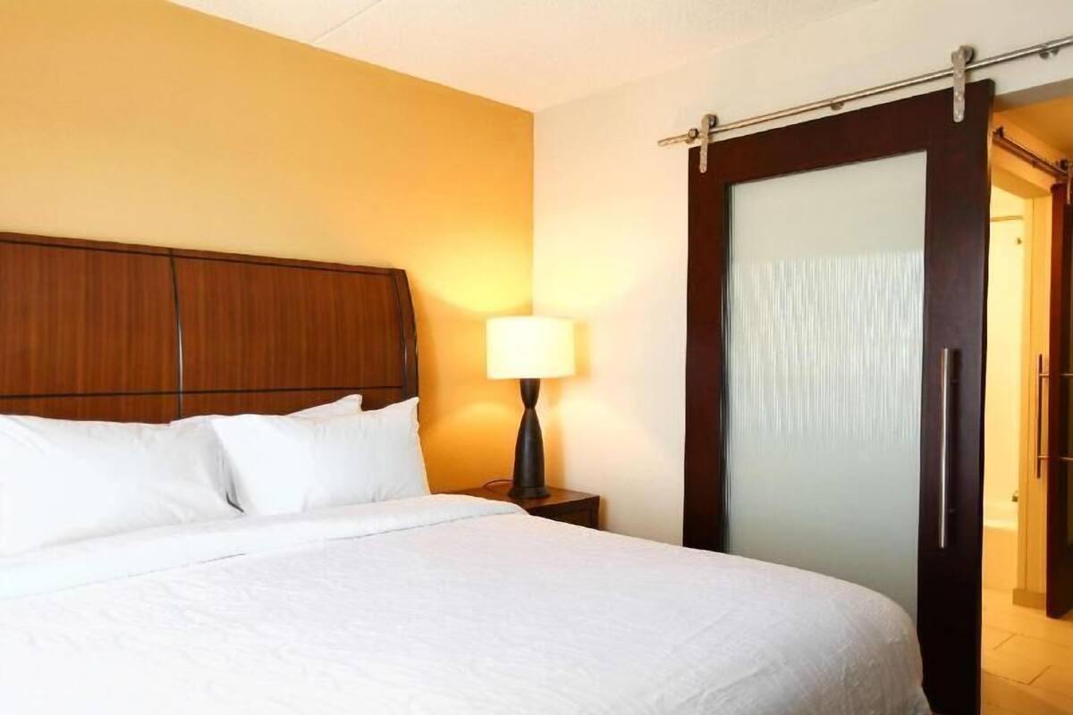 A hotel room with a bed, a nightstand, a lamp, and a sliding door.