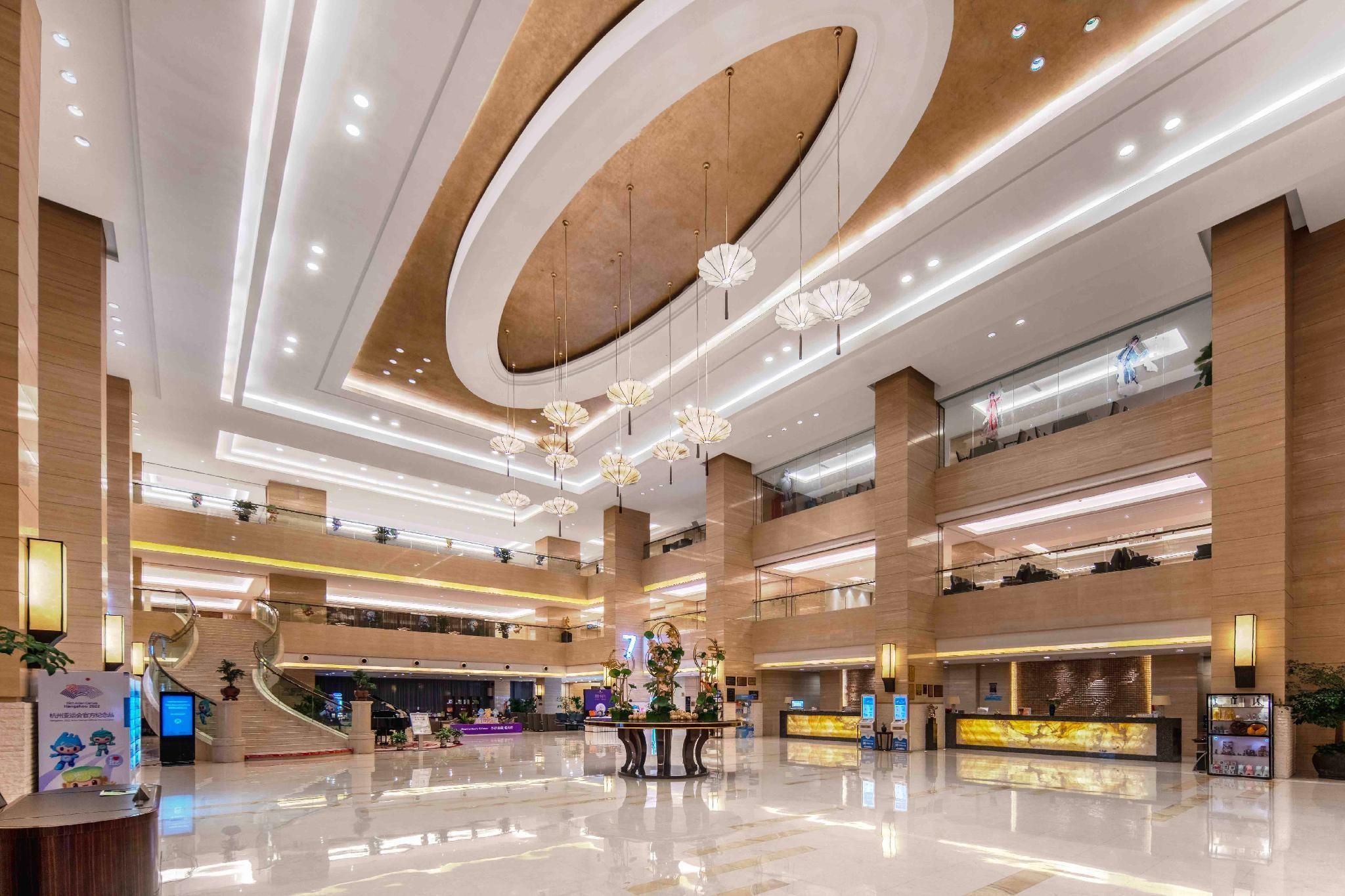 A spacious lobby with a central reception desk, multiple floors, and a modern ceiling design.