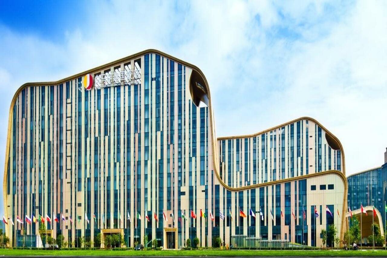A modern building with vertical windows and a curved facade, surrounded by multiple flags.