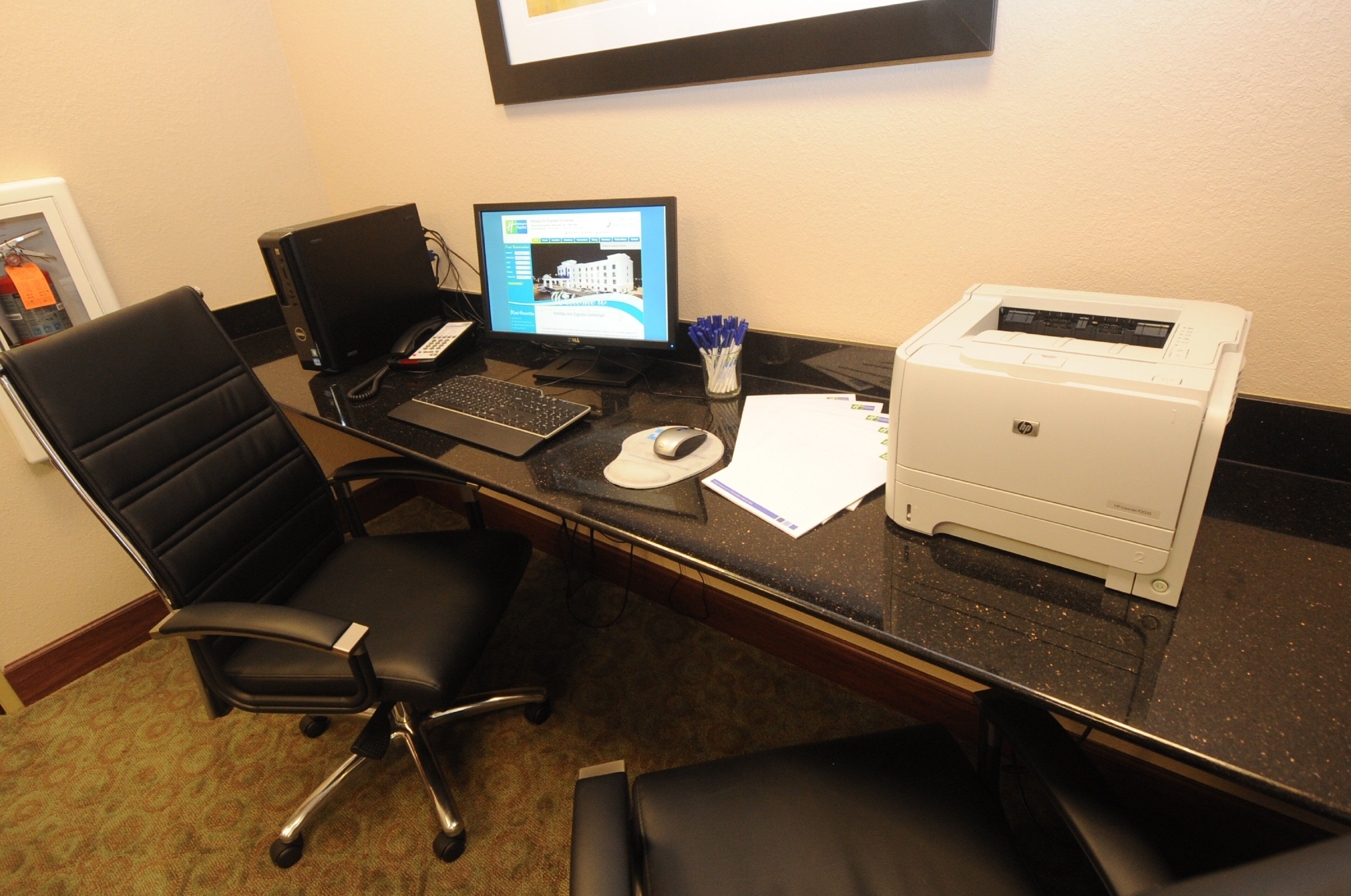 A hotel office with a desk, computer, printer, and two office chairs.