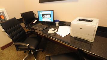 Una oficina de hotel con un escritorio, computadora, impresora y dos sillas de oficina.
