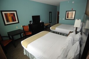 Habitación de hotel con dos camas, un escritorio, una silla, un televisor y obras de arte en las paredes.