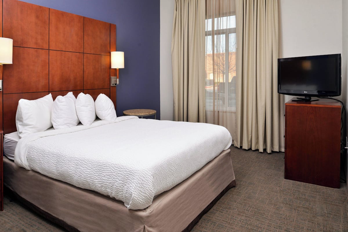 A hotel room with a large bed, a television on a wooden stand, and a window with curtains.