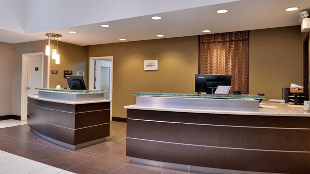 A reception desk with a glass top and a digital screen, a sign above it, and a patterned wall behind. - Residence Inn by Marriott Coralville (Coralville)