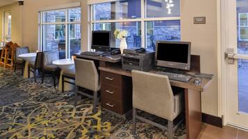 A business center with multiple computer stations, a white vase with flowers, and a view of the outside through large windows.