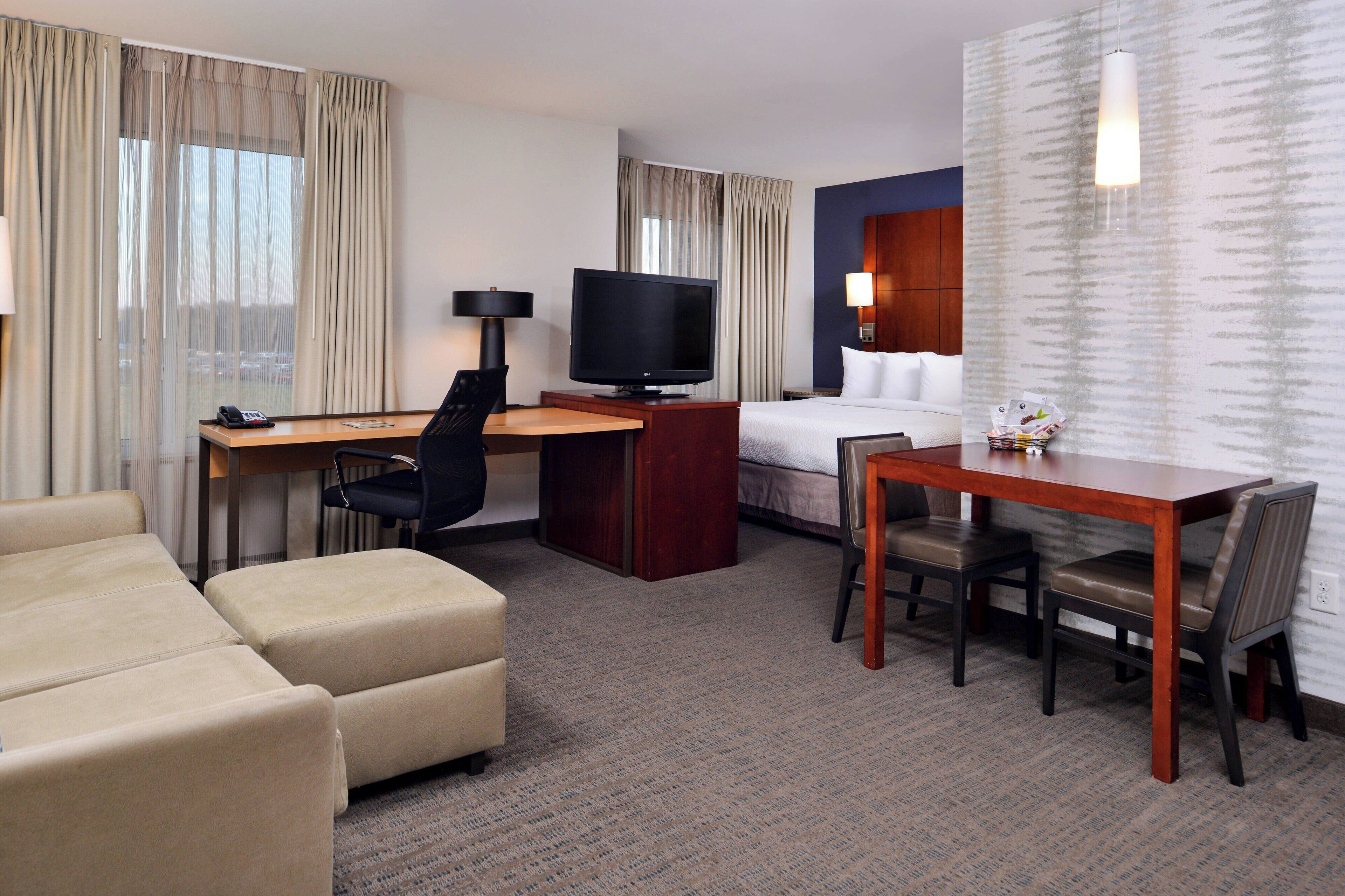 Une chambre d’hôtel comprenant un lit, un bureau avec une télévision, une table à manger avec des chaises et un canapé.