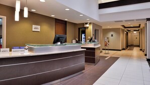 Een receptiebalie van een hotel met een modern design, een digitaal scherm en een bord met de naam van het hotel.