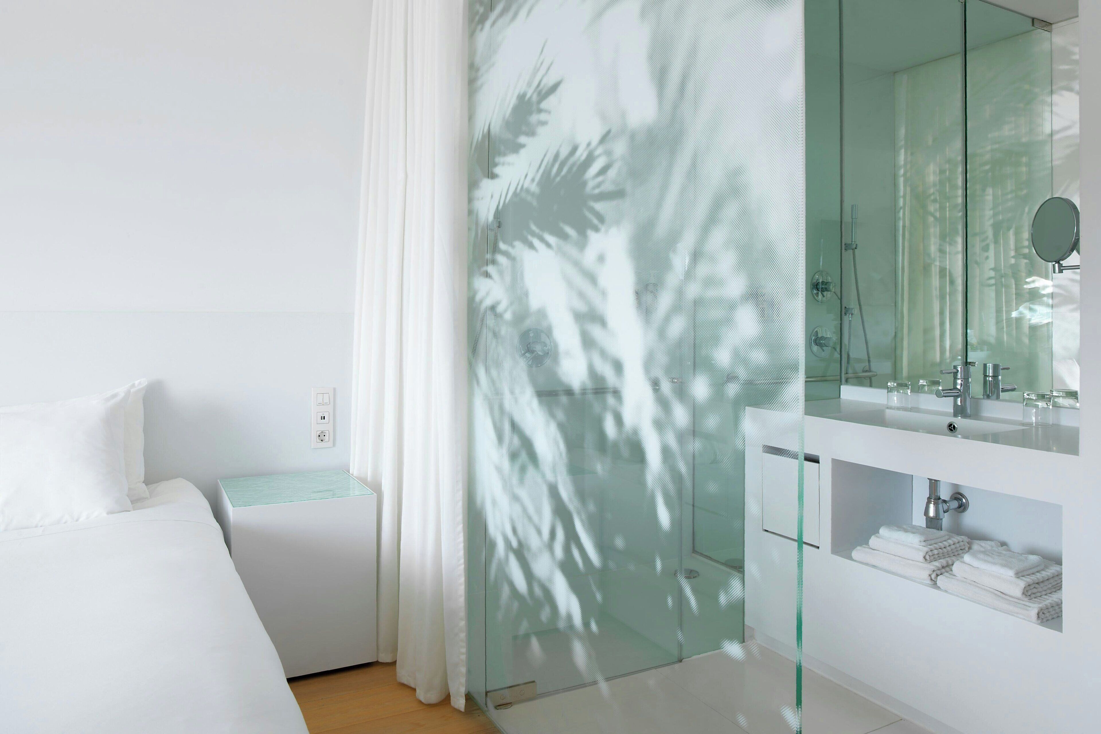 A modern hotel room with a bed, a glass shower enclosure, and a white vanity with a mirror.