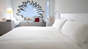 A modern hotel room with a large bed, a desk, a chair, a lamp, and a decorative wall piece.