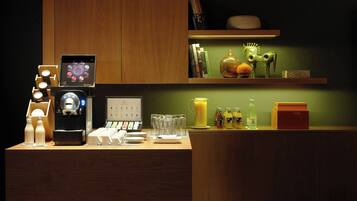 A hotel reception area with a coffee machine, a digital display, and a variety of amenities including a fruit bowl, bottles, and a calendar.
