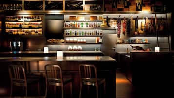 A bar area with multiple shelves of bottles, a central bar counter, and wooden chairs.