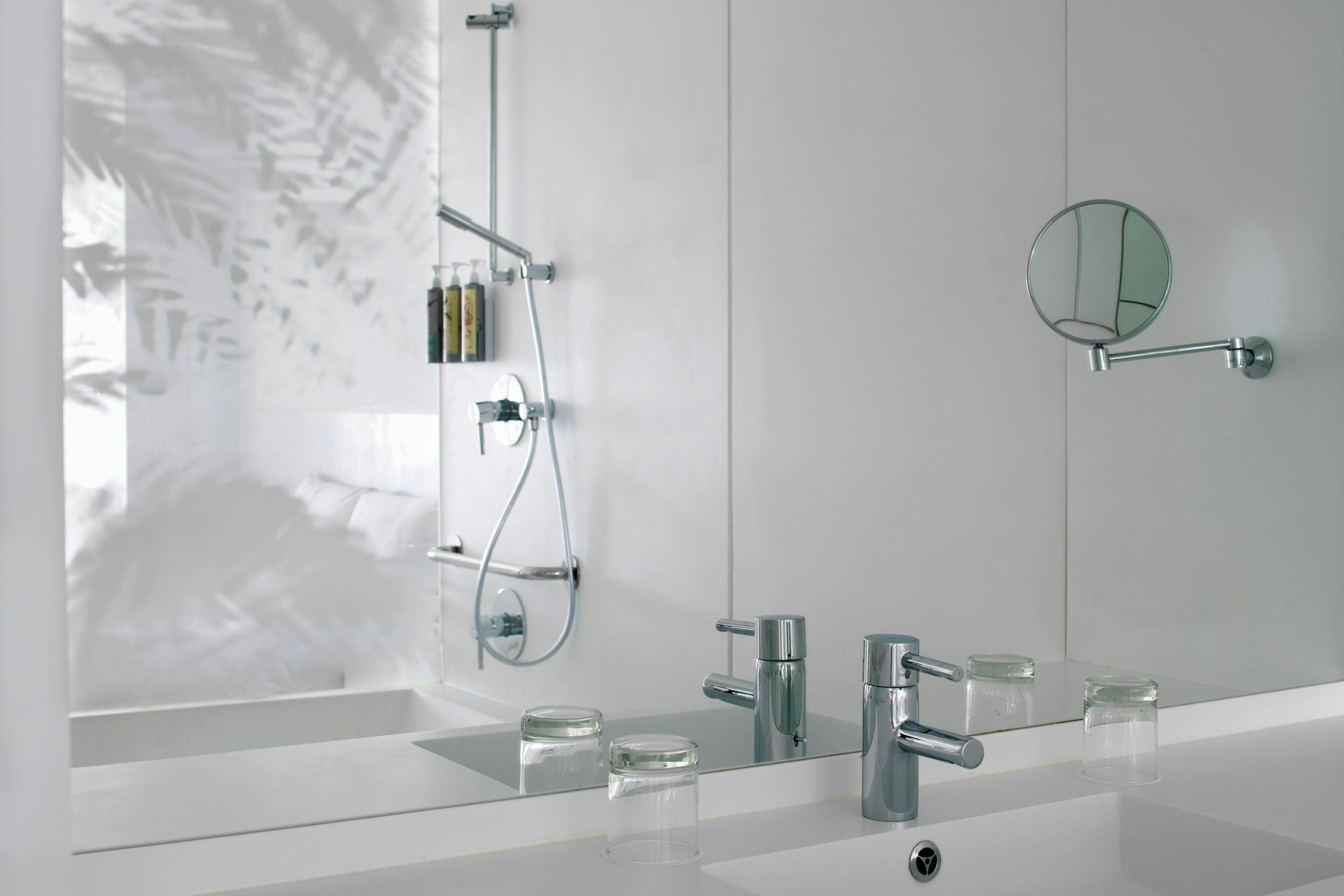 Et moderne badeværelse med et glasbadekar, et stort spejl og et hvidt toiletbord med vask og to glasbeholdere.