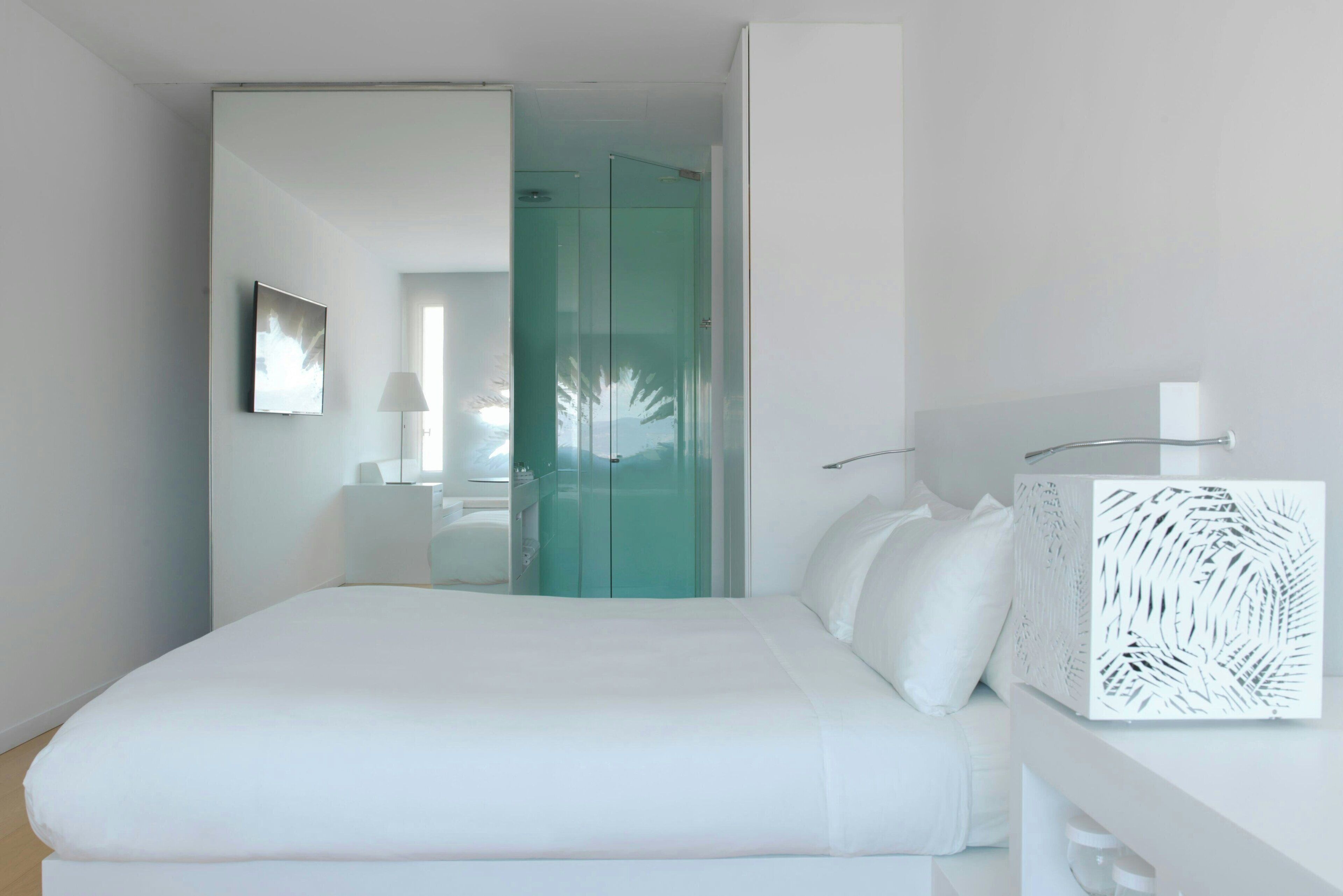 Une chambre d’hôtel moderne dotée d’un grand lit, d’une armoire à portes vitrées, d’une table de chevet agrémentée d’un objet décoratif et d’une lampe fixée au mur.