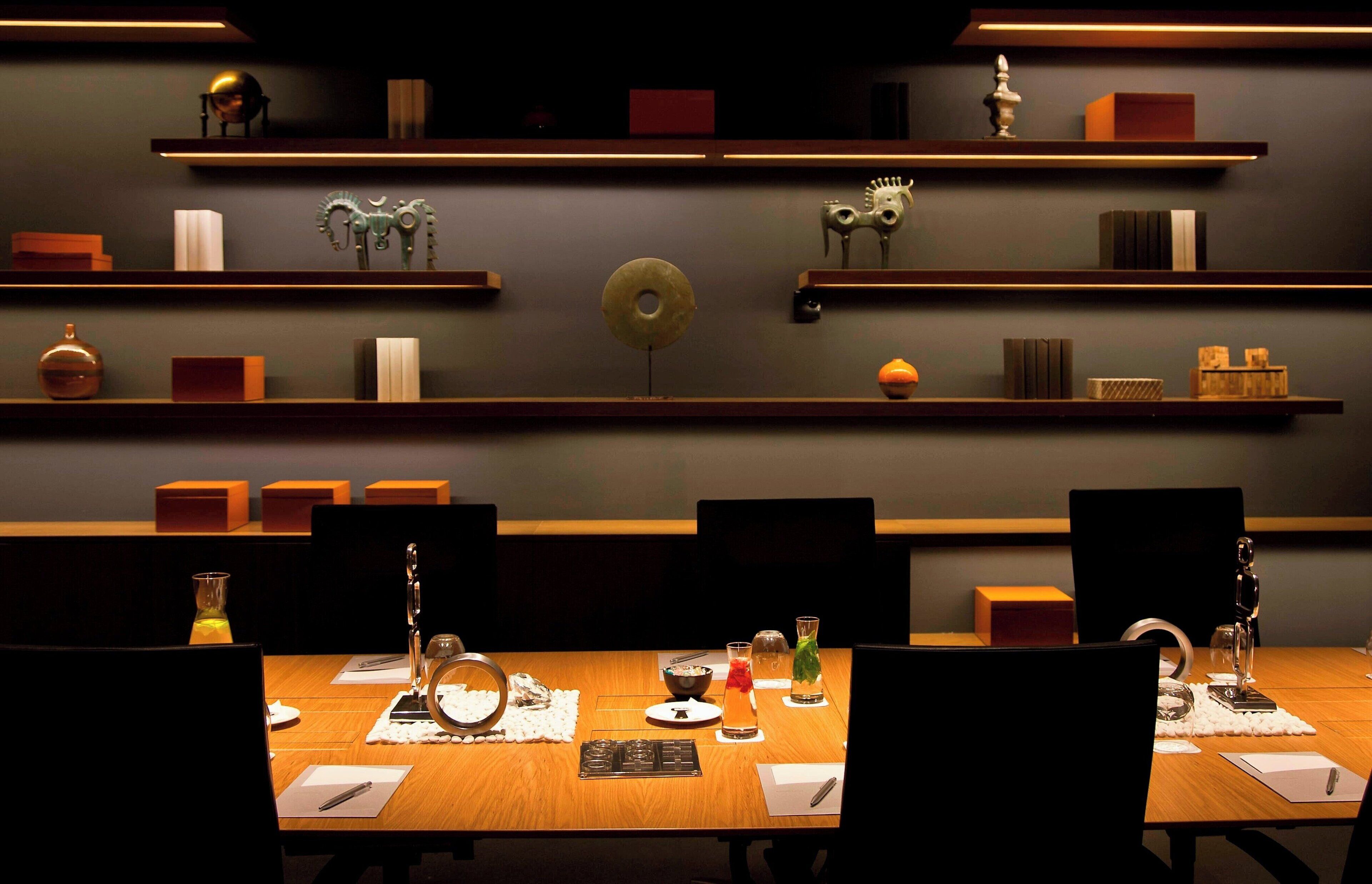 Une salle de conférence avec une longue table, des chaises et des étagères ornées de divers objets décoratifs.