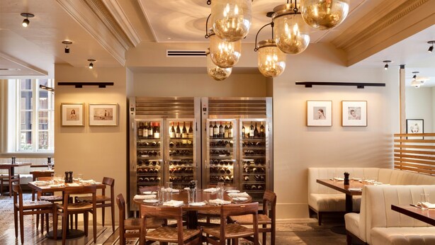 A dining area with wooden tables and chairs, a wine cellar with wine racks, and a seating area with cushioned sofas.