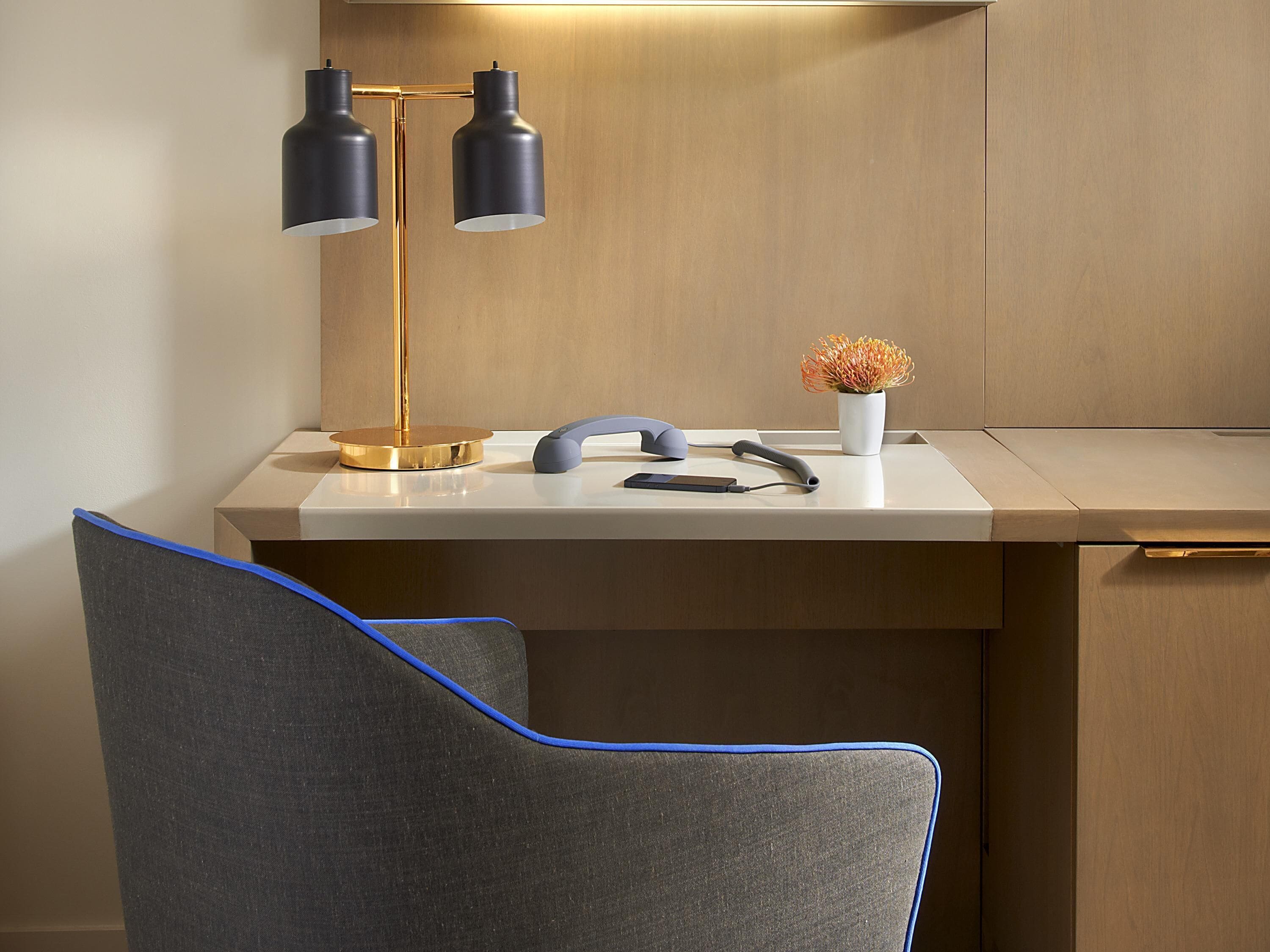 A modern desk with a gold lamp, a vase with flowers, and a smartphone.