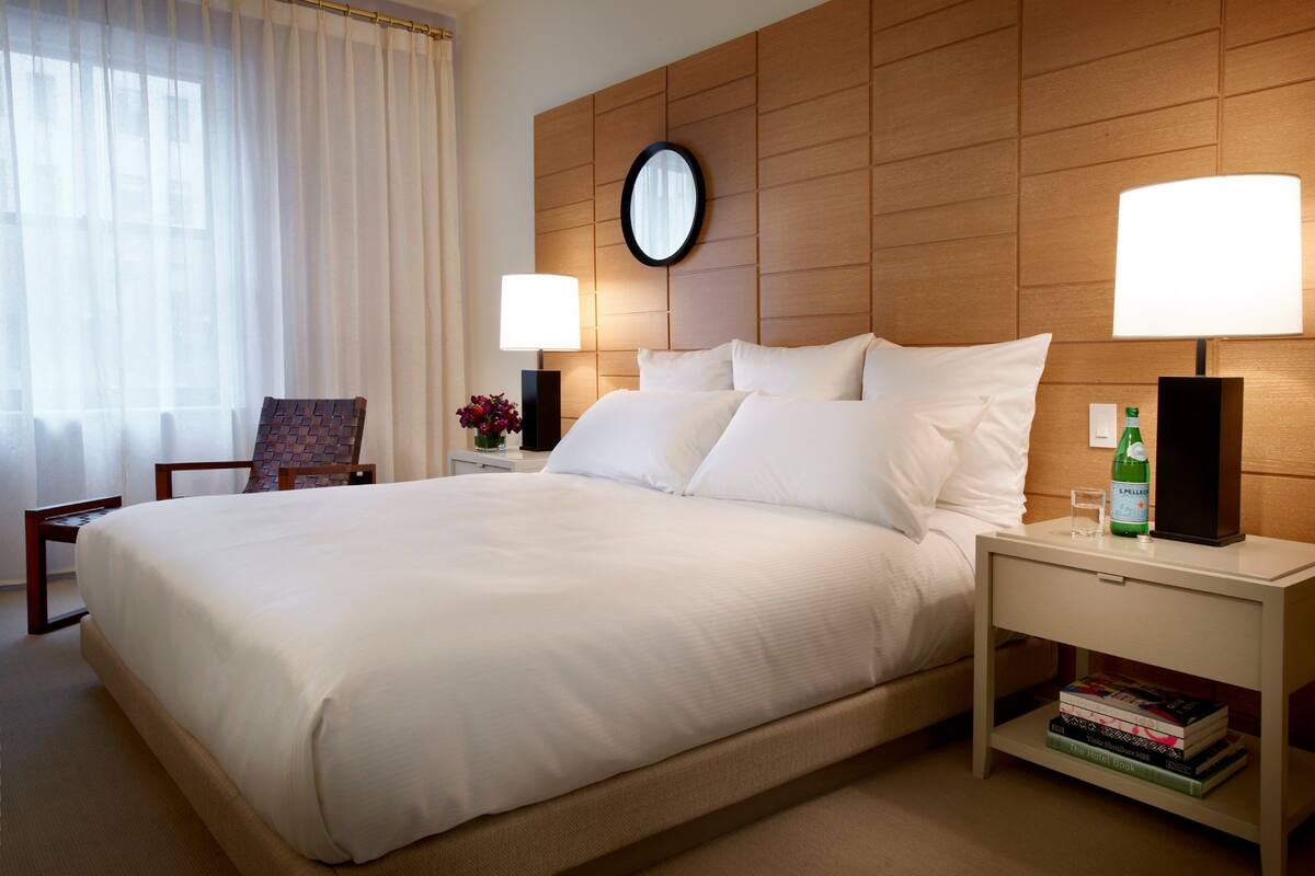 Una habitación de hotel con una cama grande, dos mesitas de noche con lámparas, una silla y un reloj en la pared.