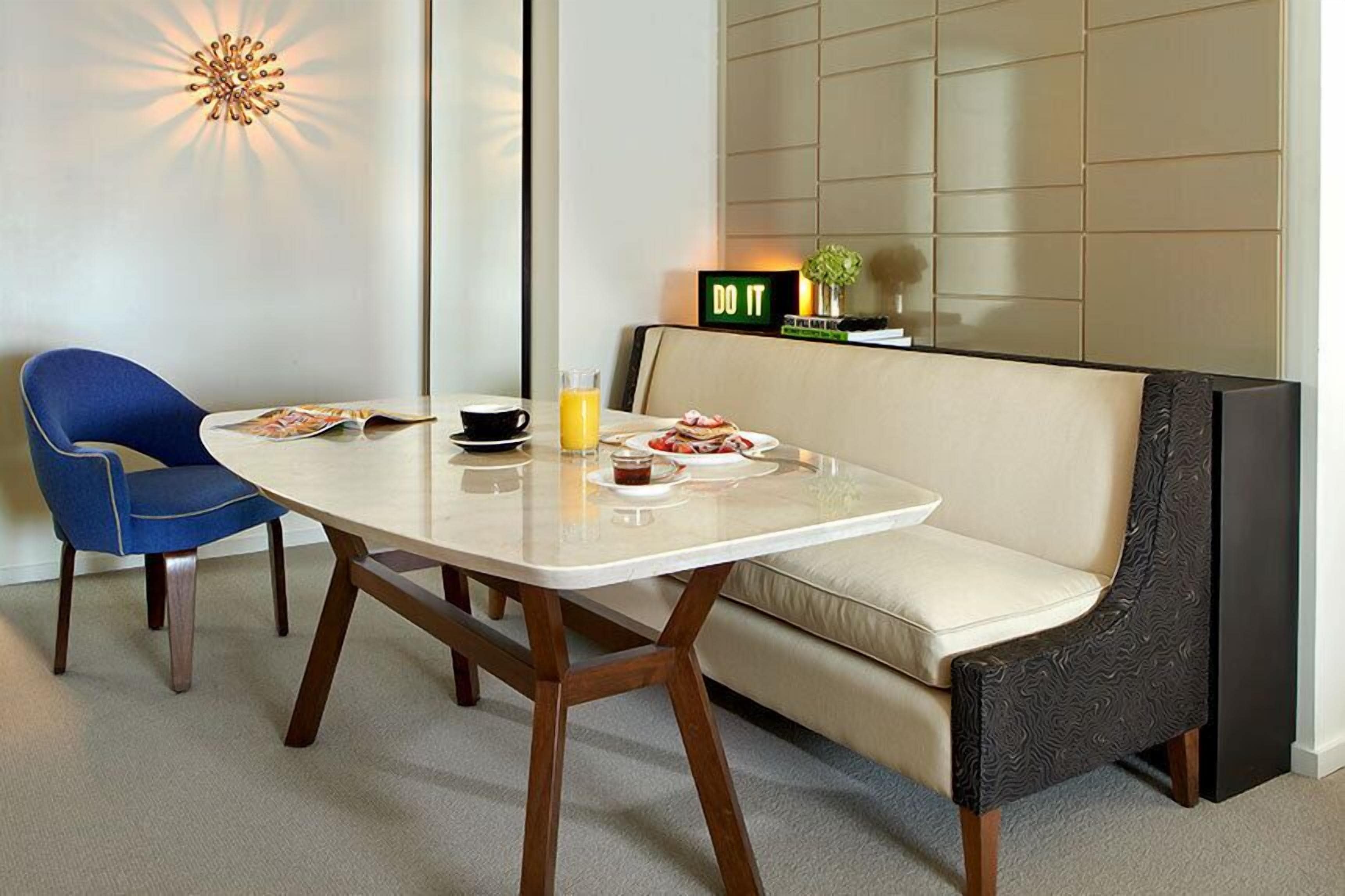 A modern dining area with a glass table, two chairs, a sofa, and a 'DO IT' sign on the wall.