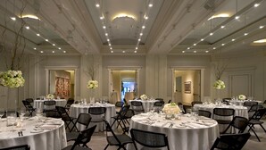 A large banquet hall with round tables, black chairs, and white tablecloths.