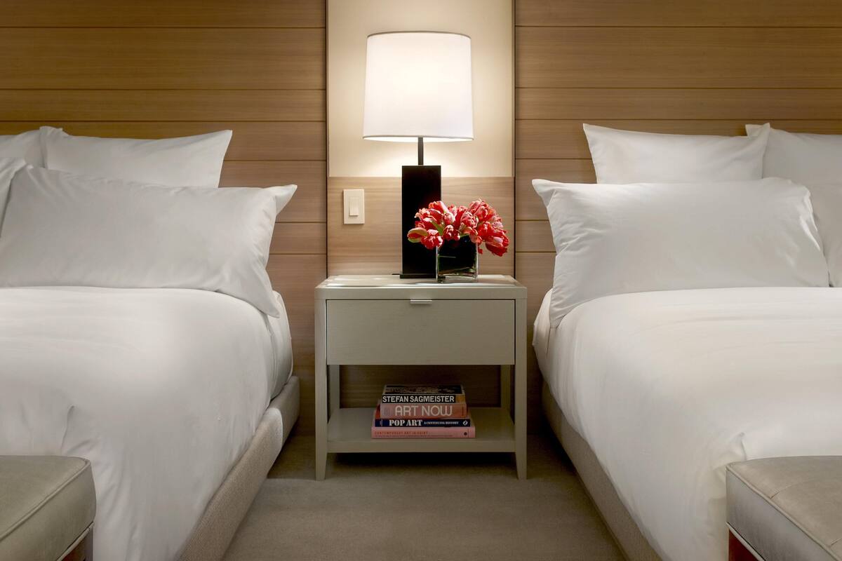 Una habitación de hotel con dos camas, una mesita de noche con lámpara y un jarrón con flores.