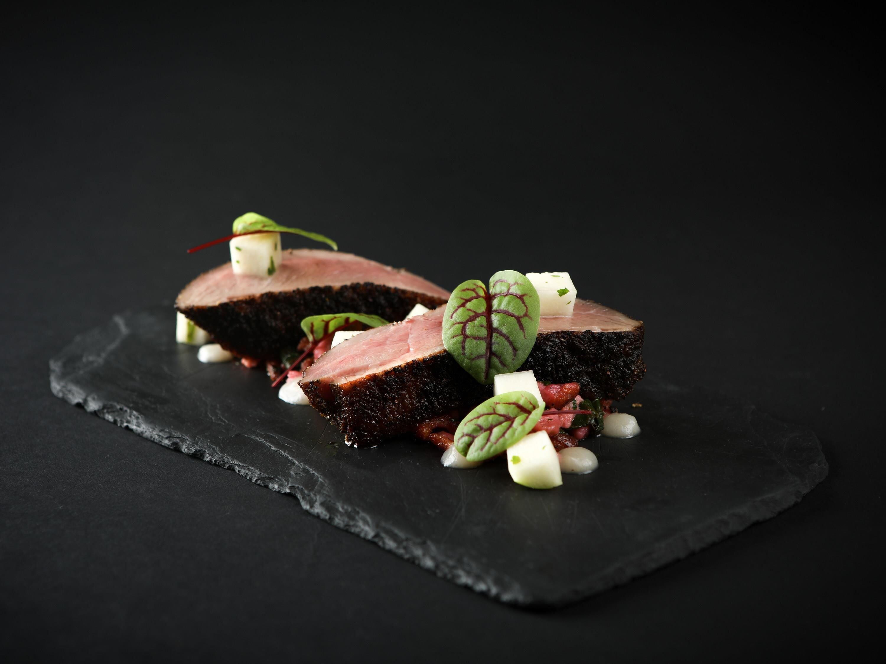 A black slate serving board with a piece of meat and garnishes.