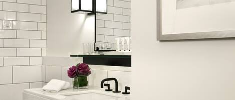 A modern bathroom with a white tiled wall, a white sink with a black faucet, a black towel rack, and a framed artwork above the mirror.