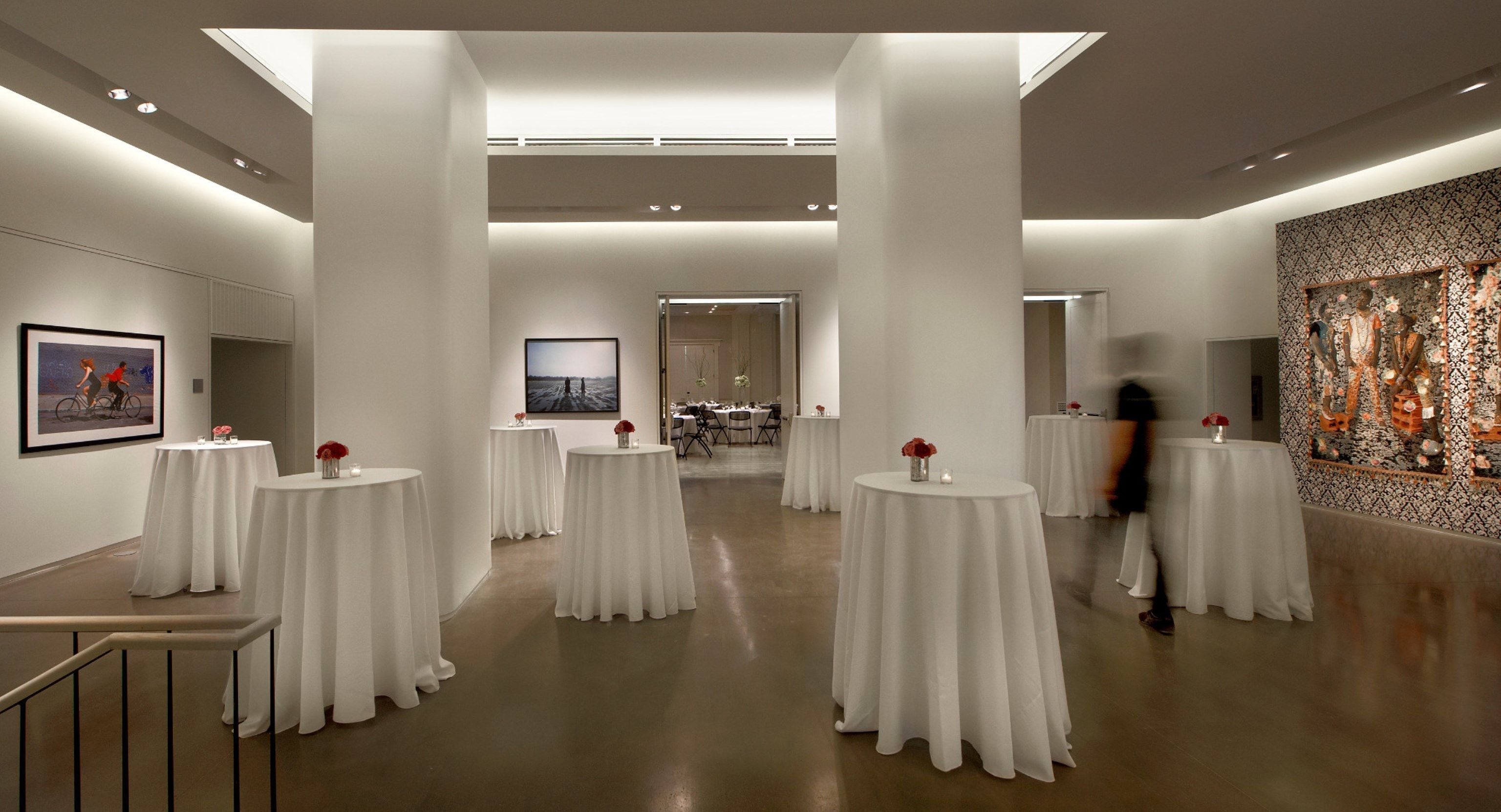 Una galería amplia y bien iluminada con mesas blancas y un espacio central abierto.