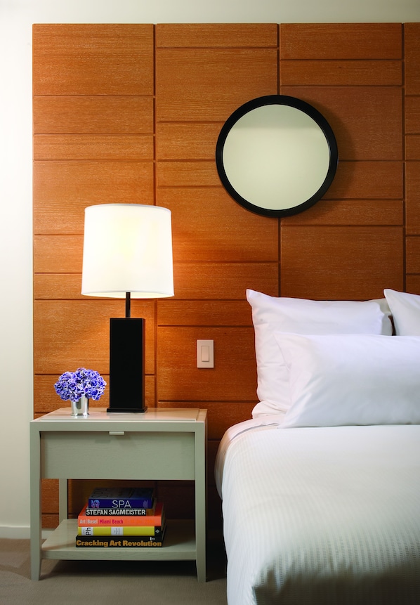 A neatly arranged hotel room with a wooden headboard, a bedside lamp, a small table with a vase of flowers, and a stack of books. - 21c Museum Hotel Cincinnati (Cincinnati)