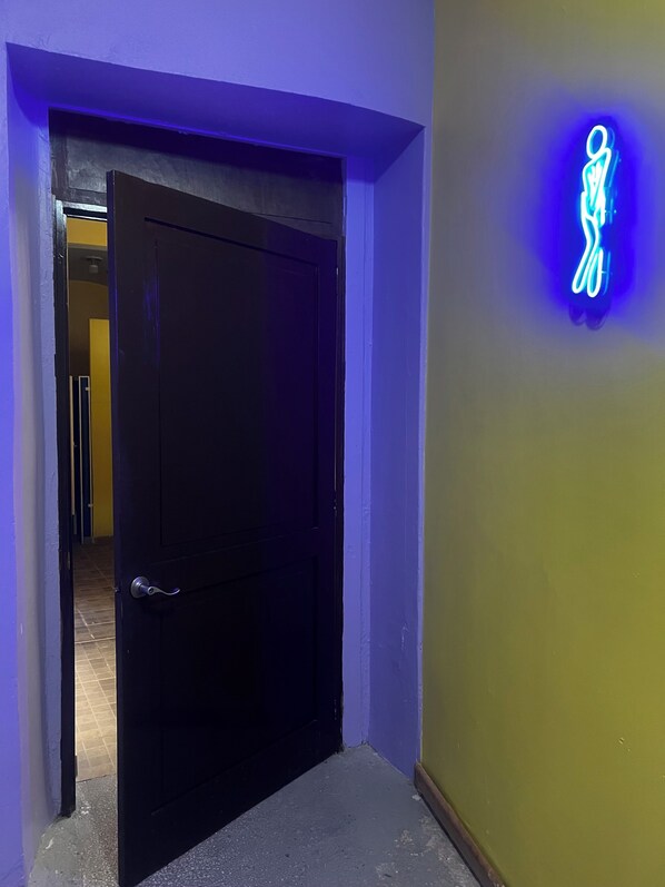 A hallway with a closed door, a neon sign on the wall, and a tiled floor. - Hostal Amigo - Hostel (Mexico City)