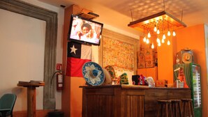 Eine Bar mit einem Wandfernseher, einer Holztheke, Barhocker und einer Deckenleuchte.