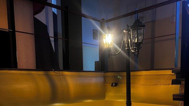 Ein schwach beleuchteter Raum mit einer hölzernen Bank, einer Pendelleuchte und einer Wandlampe.