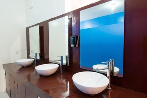 Een badkamer met drie witte wasbakken en een grote spiegel.