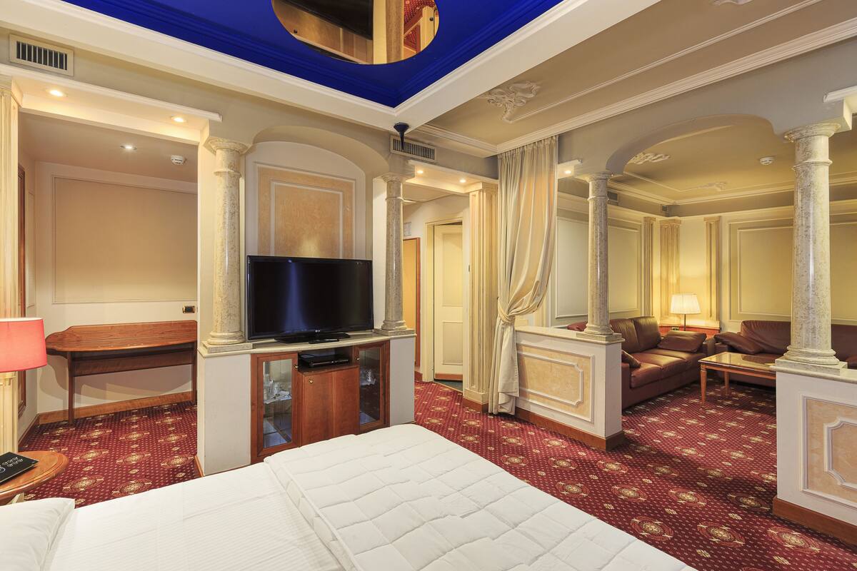 A hotel room with a large bed, a television, a desk, and a seating area with a sofa and armchairs.