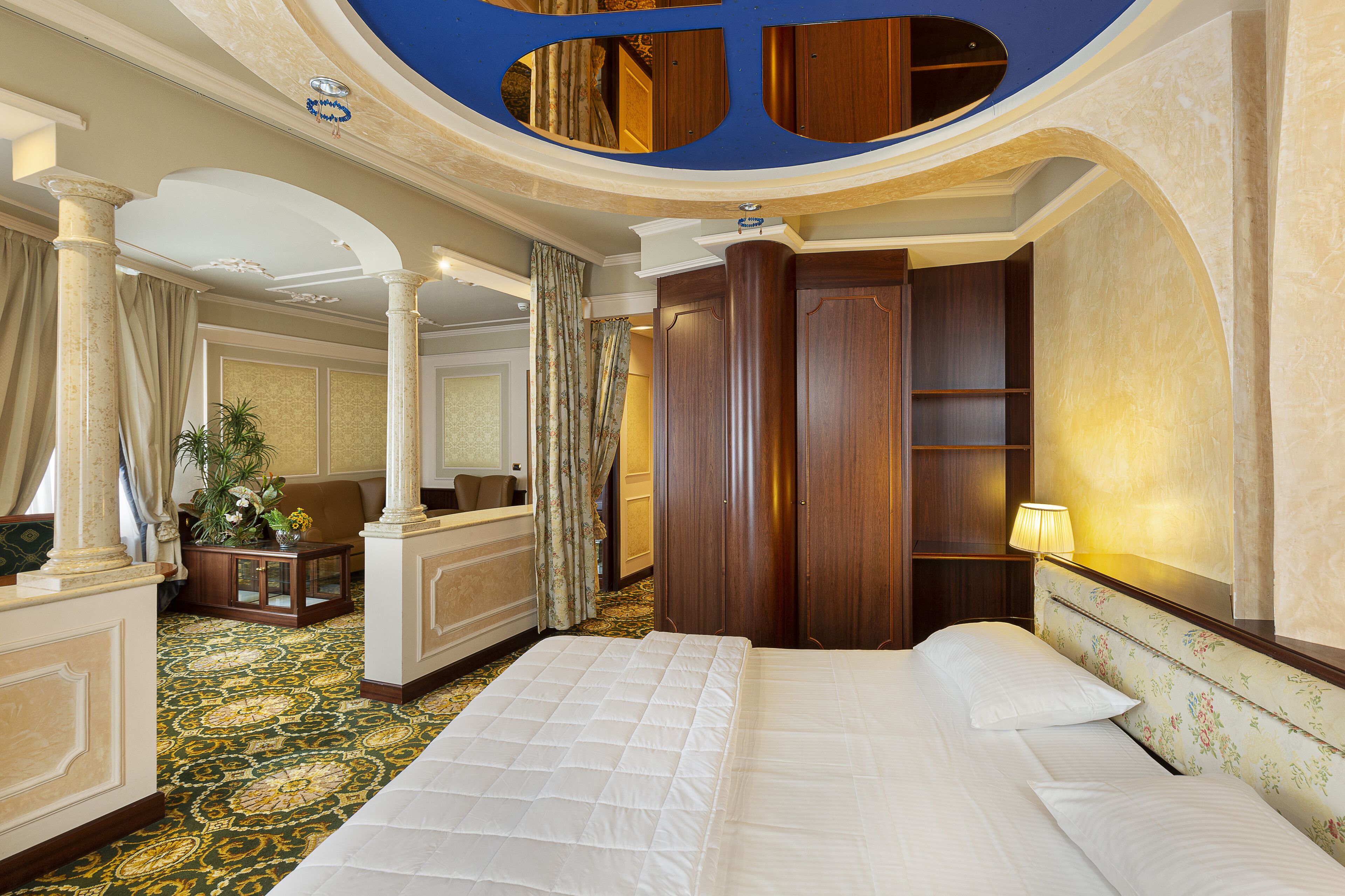 A hotel room with a large bed, a sitting area with a sofa and a small table, a mirror, and a wooden wardrobe.