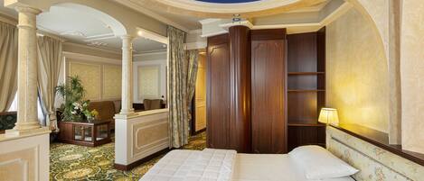 A hotel room with a large bed, a sitting area with a sofa and a small table, a mirror, and a wooden wardrobe.