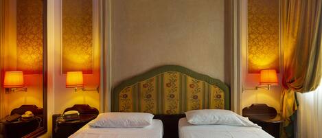 A hotel room with two beds, a large mirror, and wall sconces.