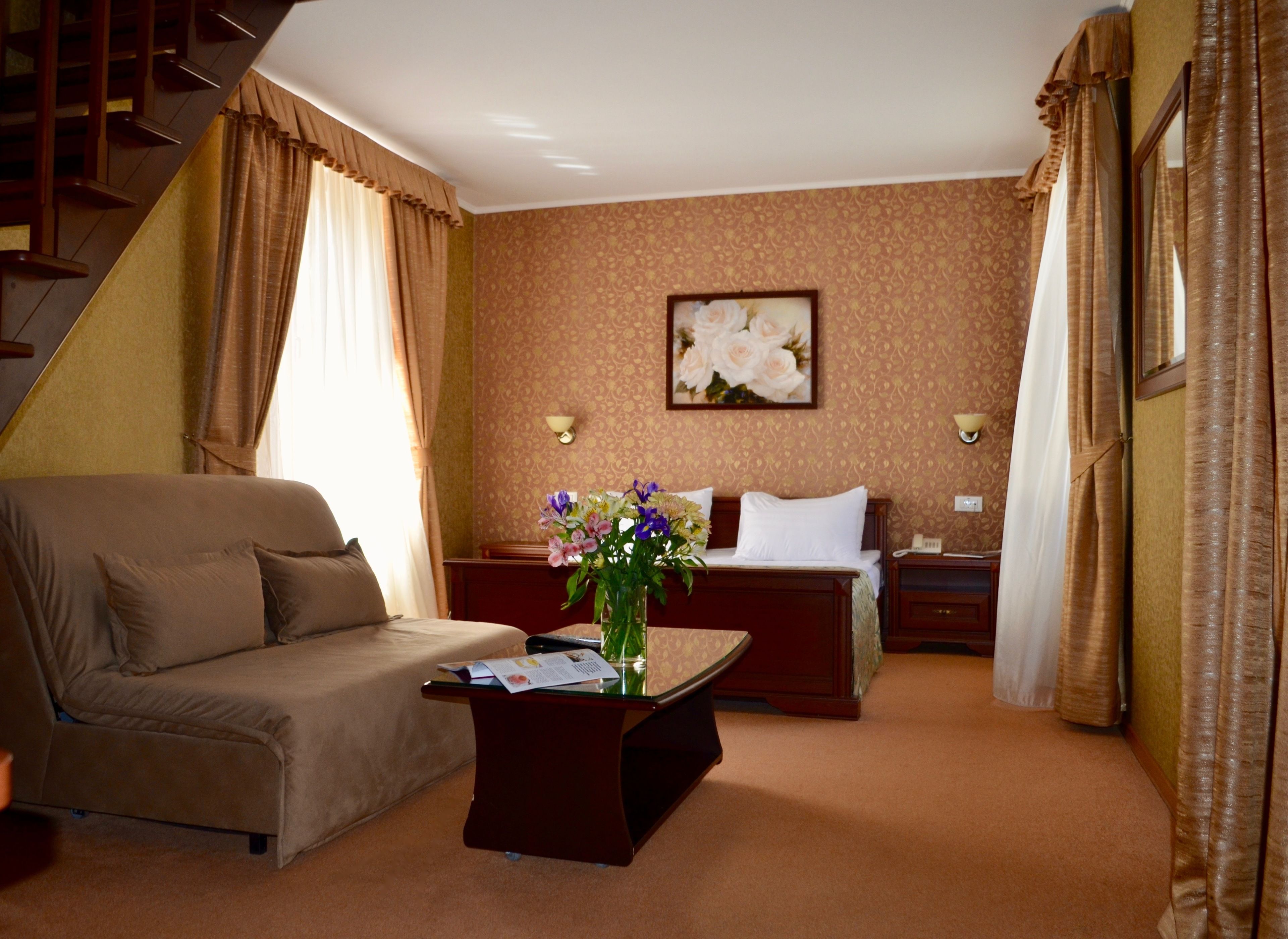 A hotel room with a sofa, a bed, a nightstand, a lamp, and a painting on the wall.