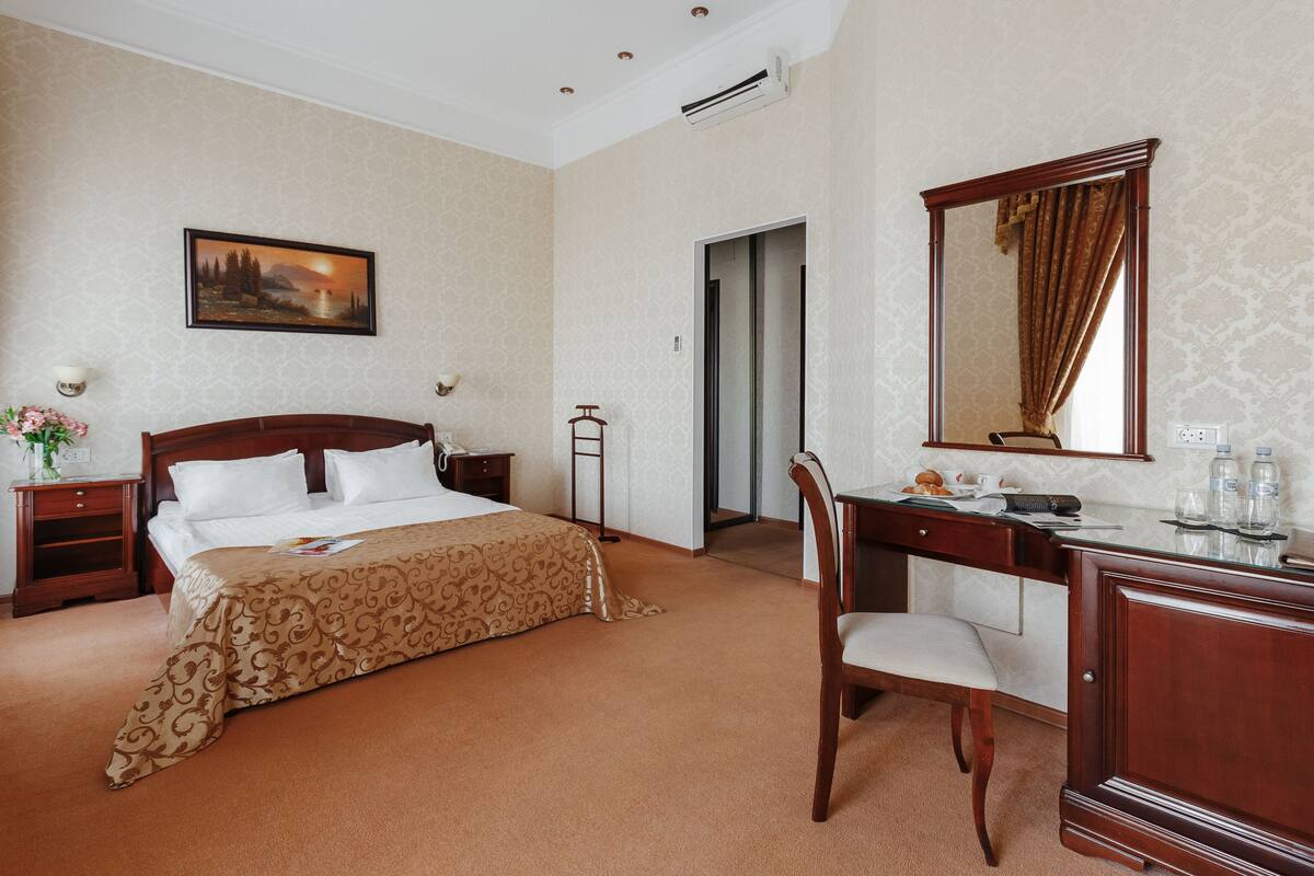 A hotel room with a bed, a desk, a chair, a dresser, a mirror, and a painting on the wall.