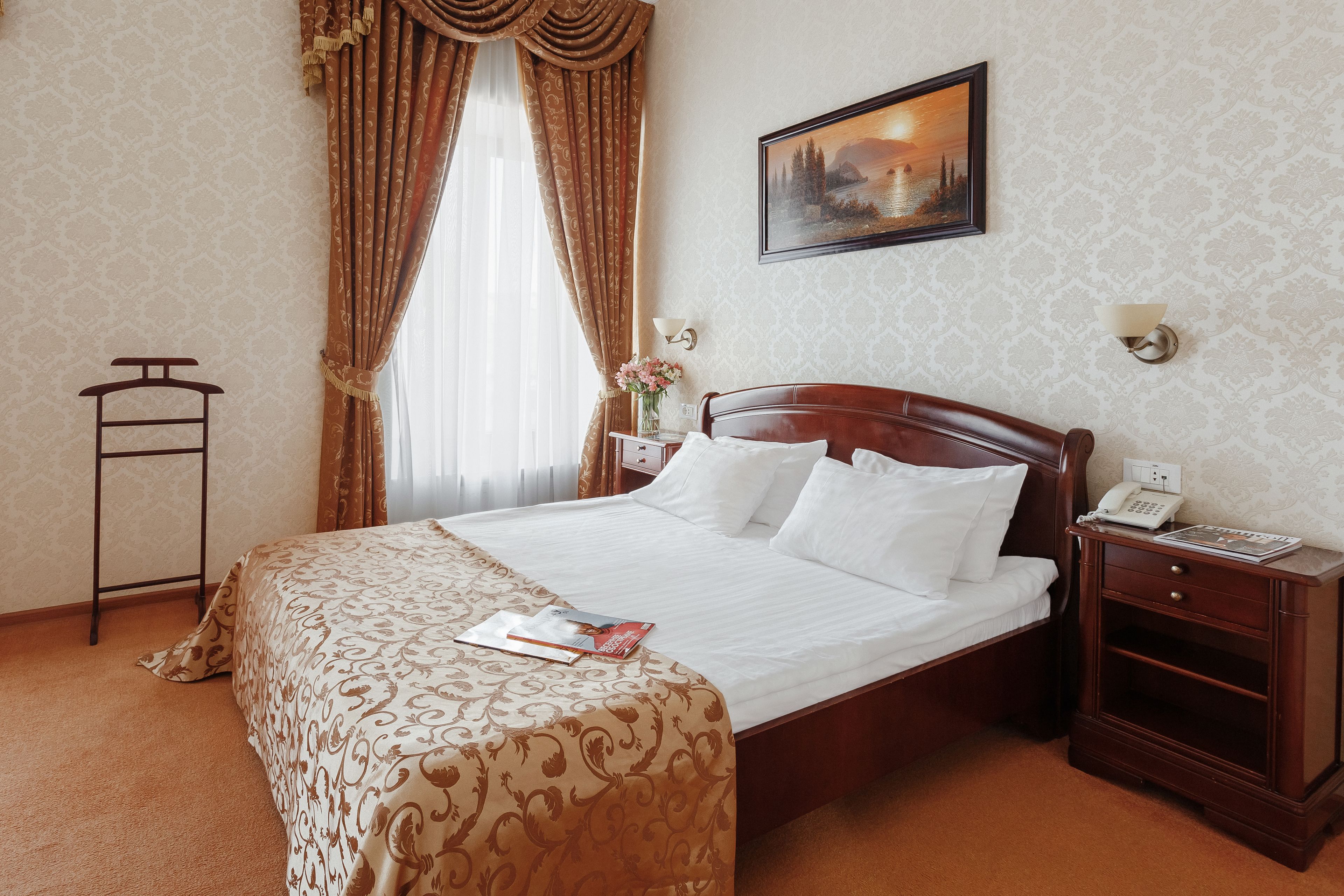 A neatly made bed with a patterned bedspread, a bedside table with a lamp, and a painting on the wall.