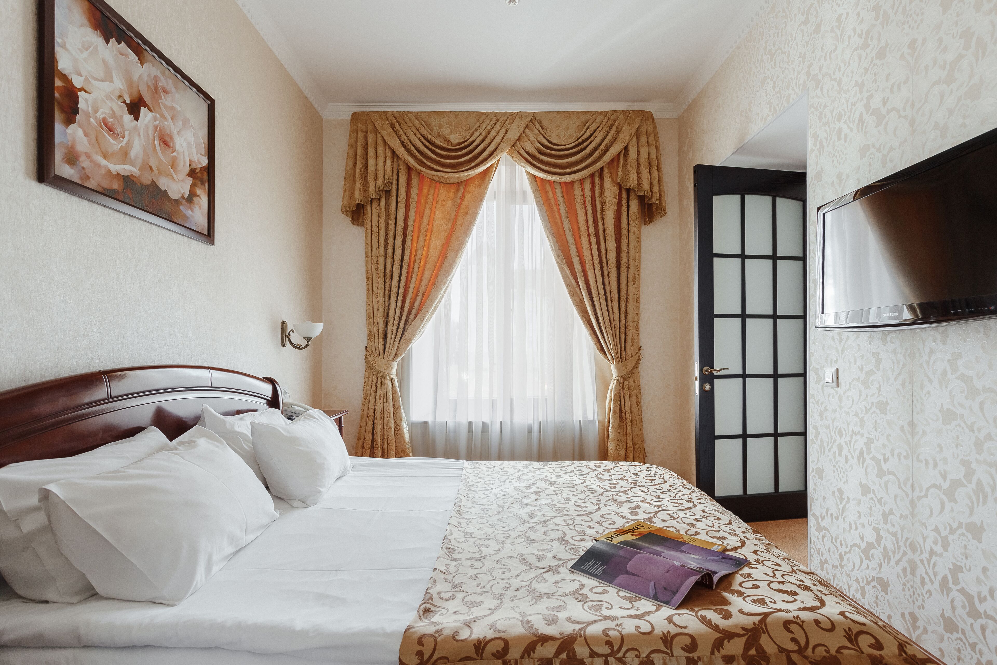 A hotel room with a bed, a television, and a door with a frosted glass panel.