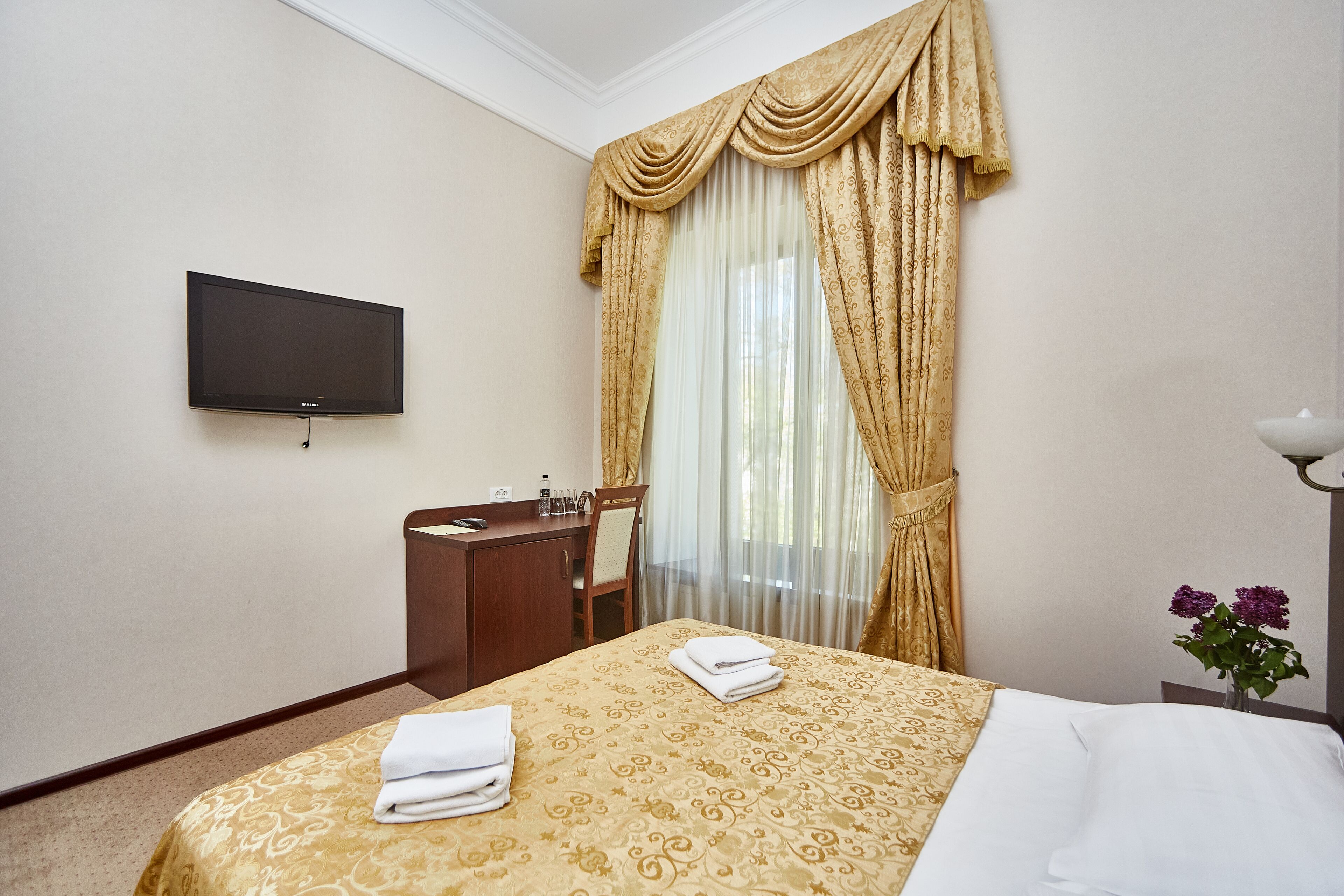 A hotel room with a bed, a desk, a chair, a television, and a window with curtains.