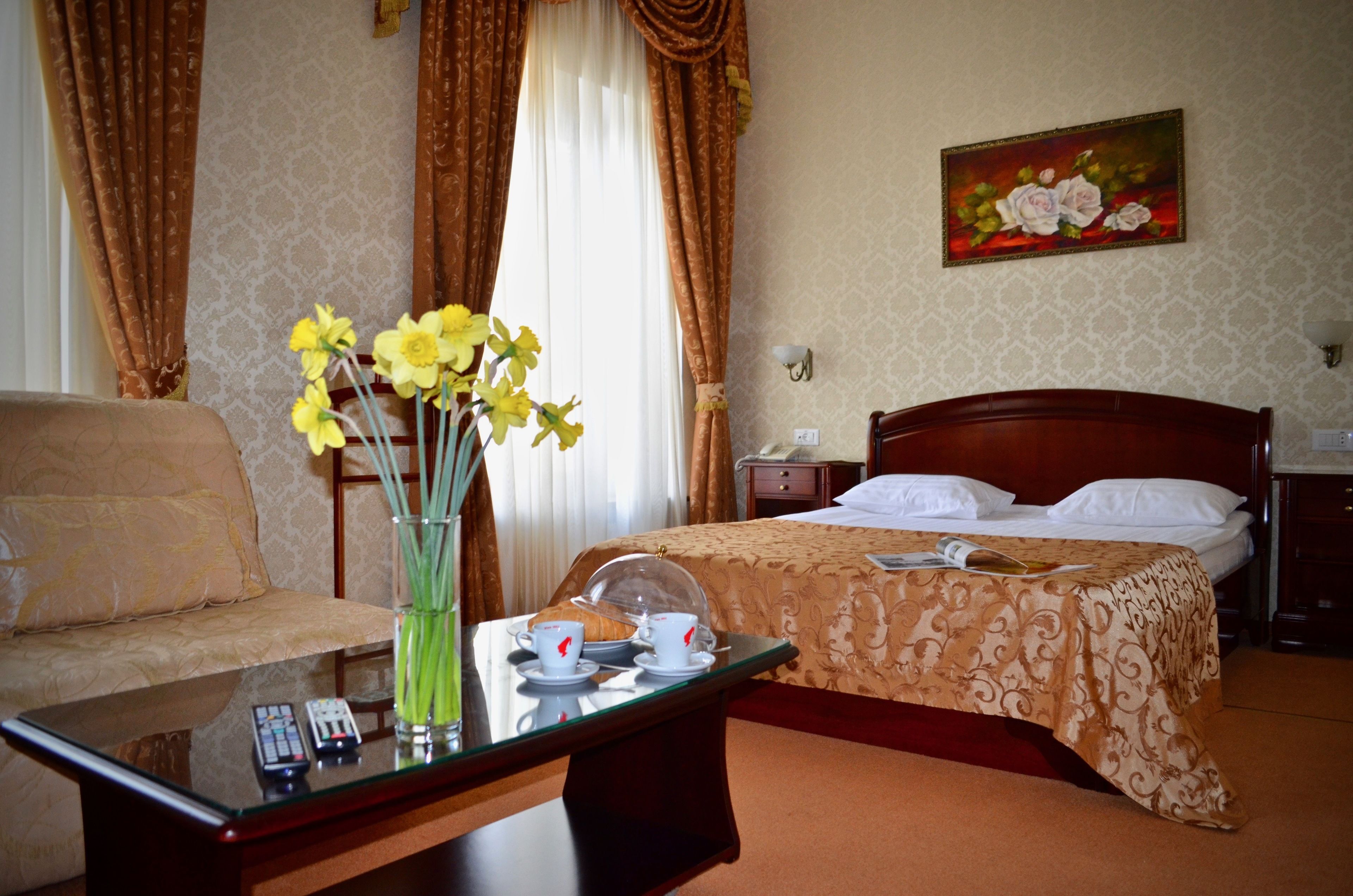 A hotel room with a bed, a sofa, a table with a vase of flowers, and a painting on the wall.