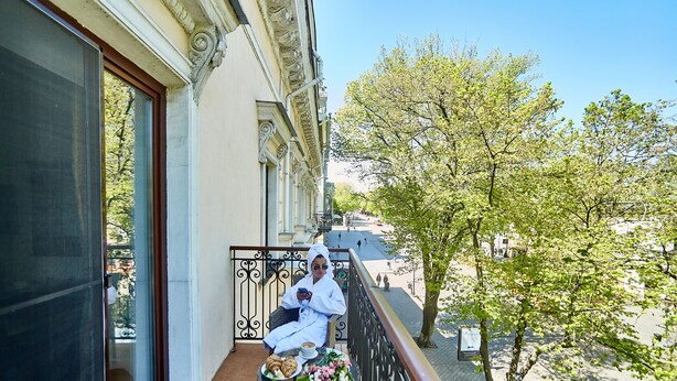 Un balcón con una mesa lista para dos personas, una silla y vista a la calle.