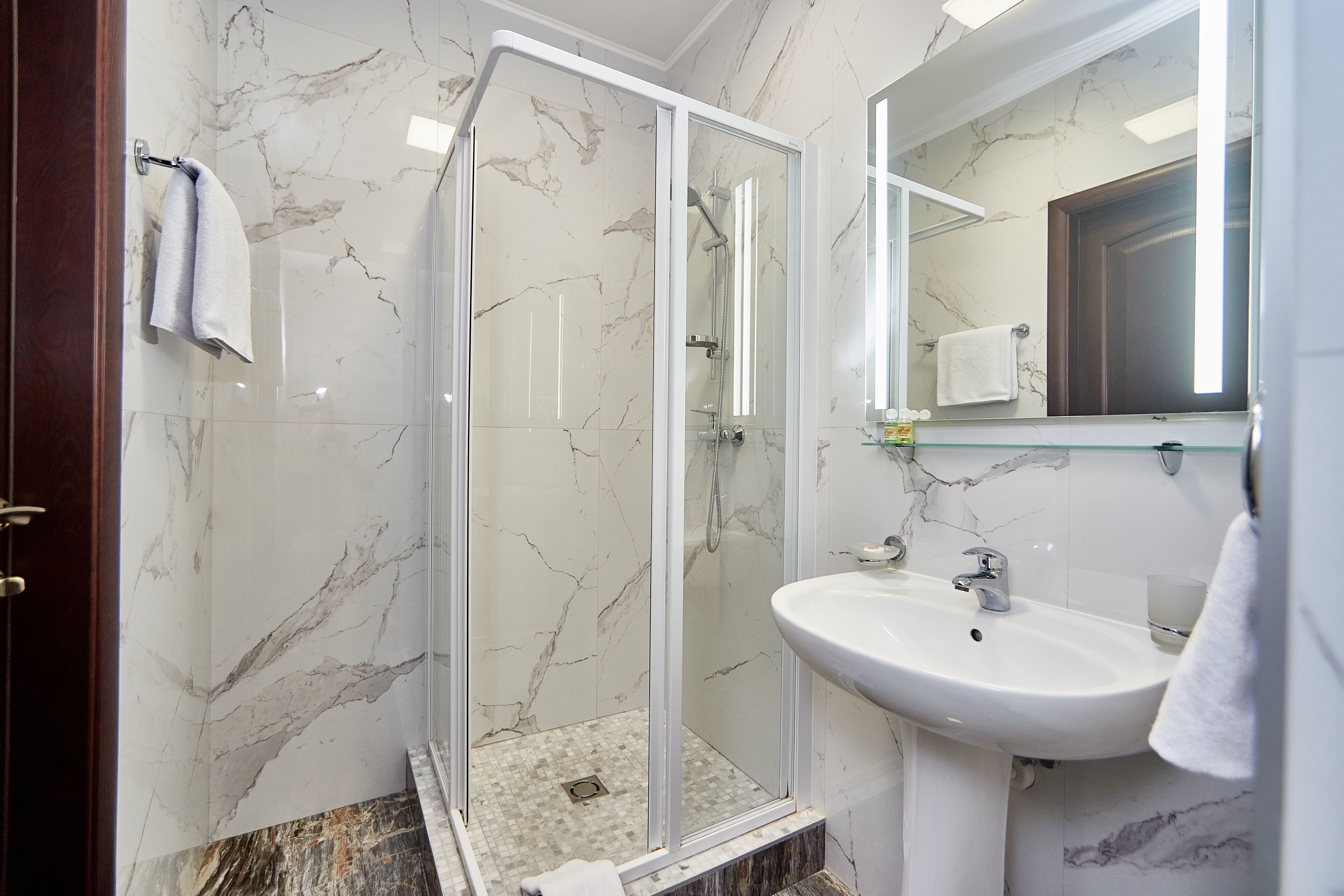 Een moderne badkamer met een douchecabine van glas, een wit wastafelmeubel en marmeren wanden.
