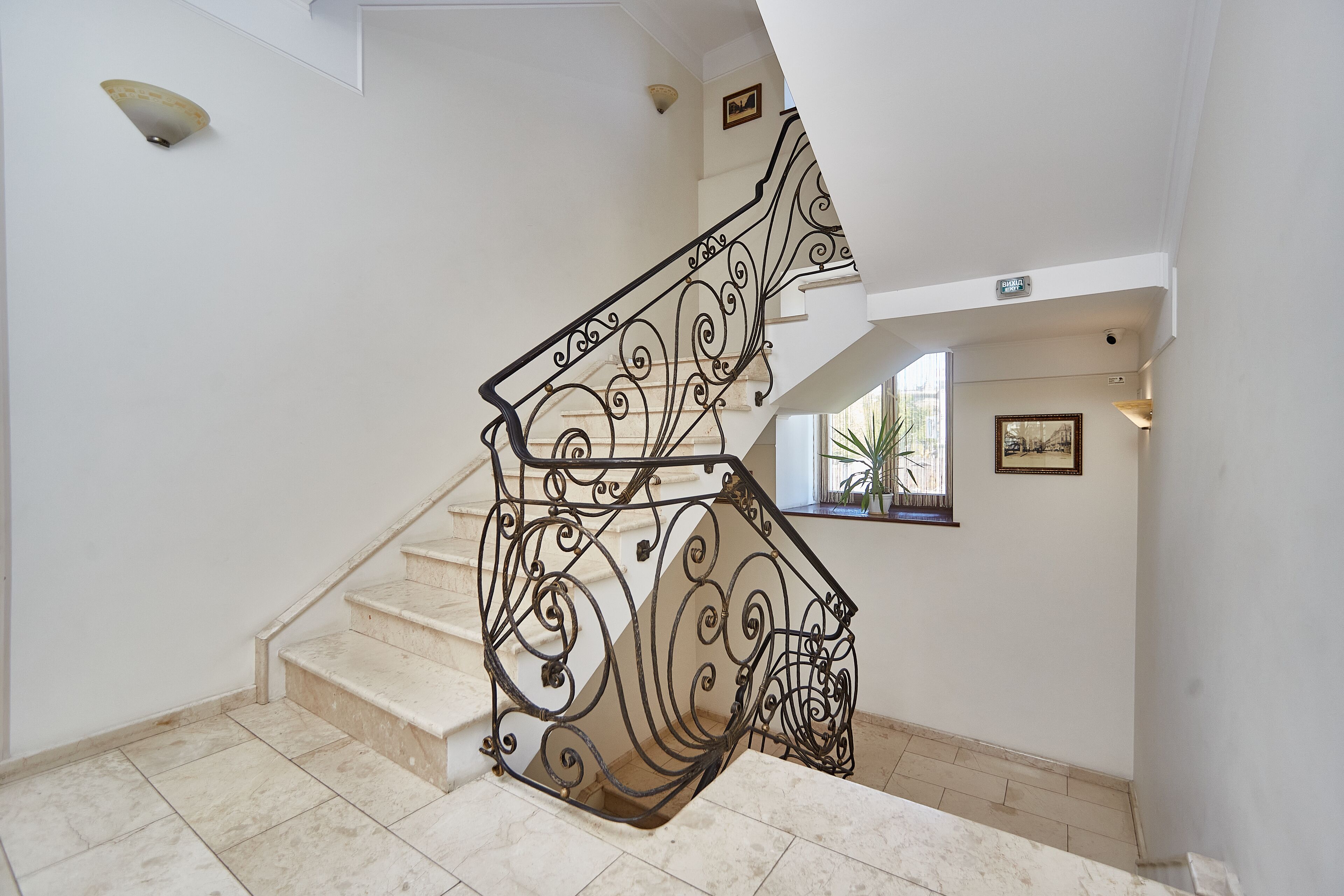 Una escalera con barandillas de metal negro ornamentado y peldaños de mármol color beige.