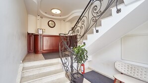 Una escalera con barandilla de hierro decorativa, una planta en maceta y un extintor.