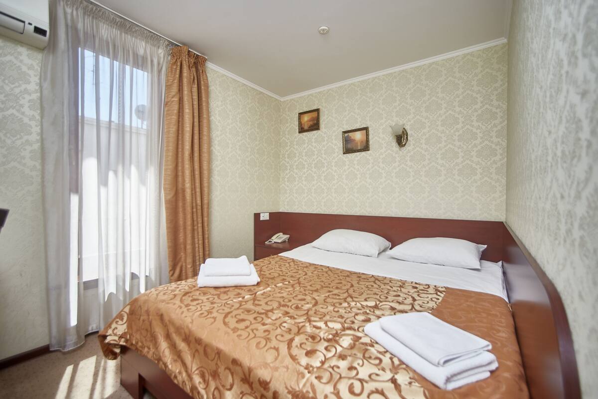 A hotel room with a large bed, a bedside telephone, and two framed pictures on the wall.