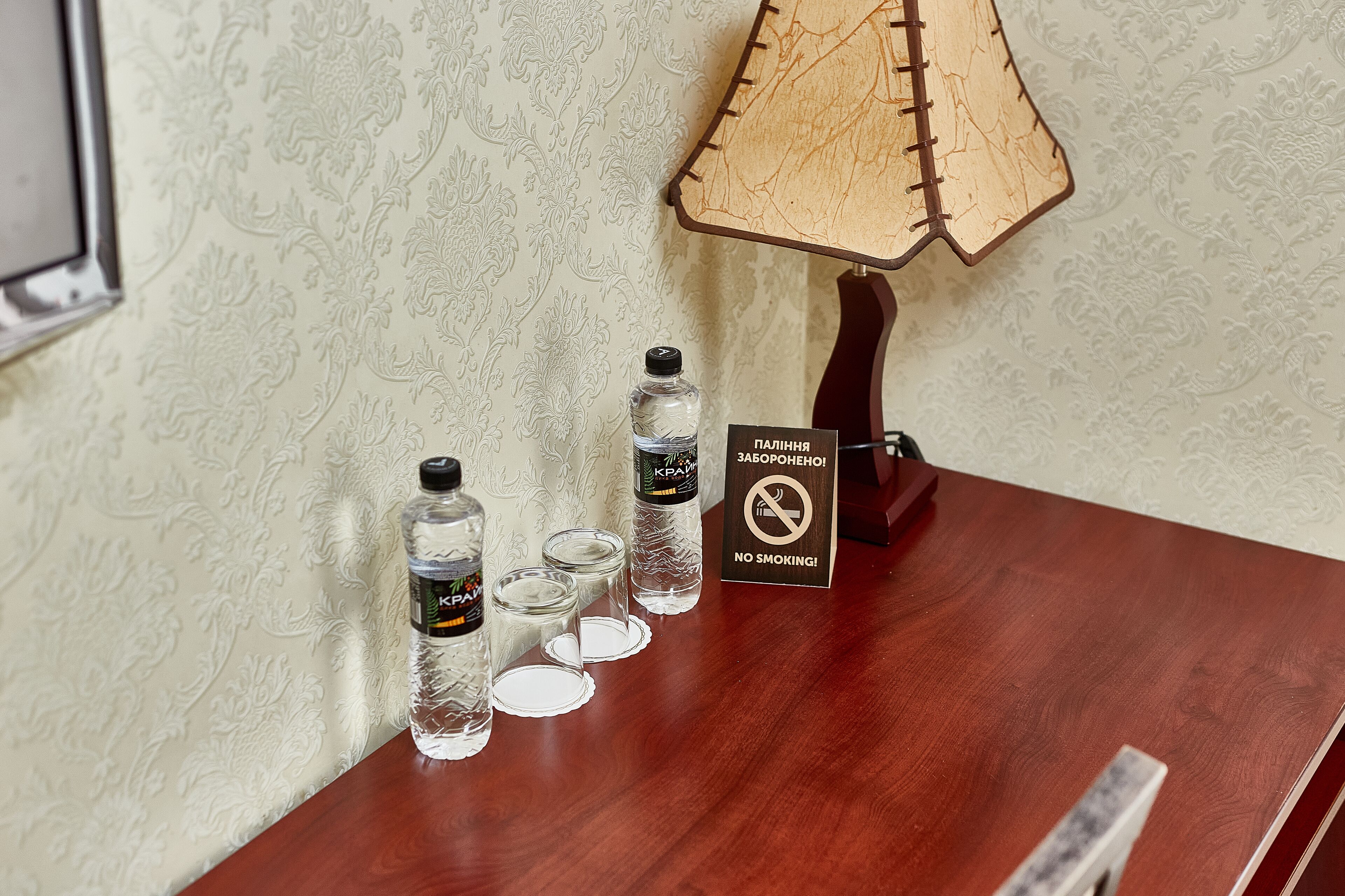 Een houten tafel met een 'Niet roken'-bord, twee waterflessen en drie glazen.